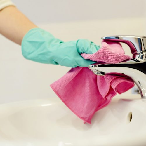 Female hands with green rubber protective gloves cleaning tap with pink cloth. Spring cleaning